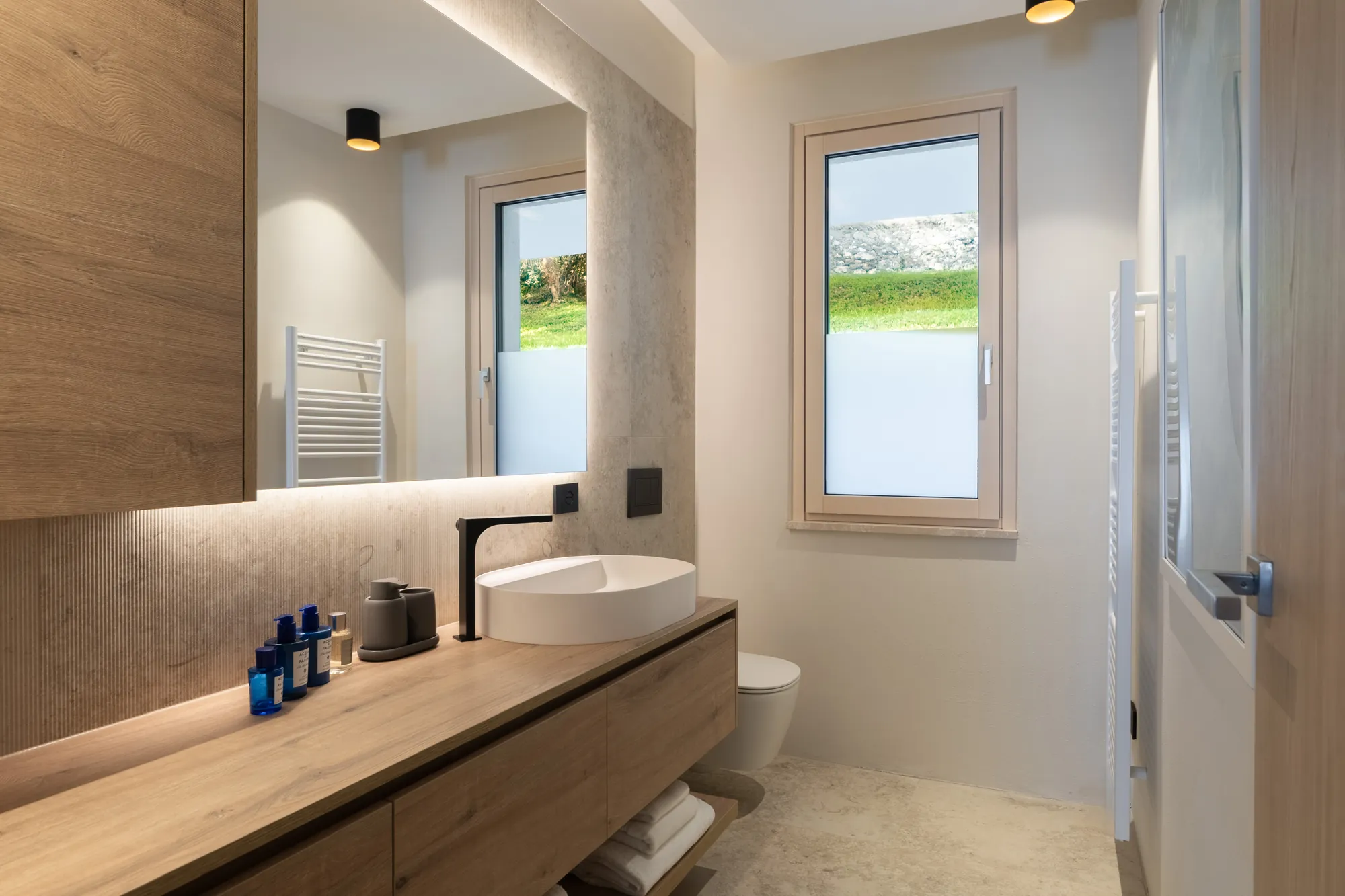 Bathroom with long oak vanity, backlit mirror and garden window