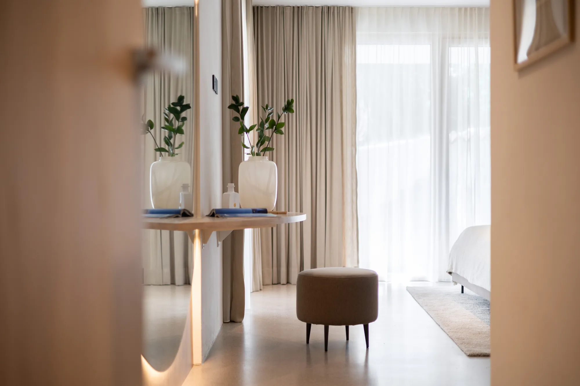 View through the doorway into a bedroom with dressing table and pouf