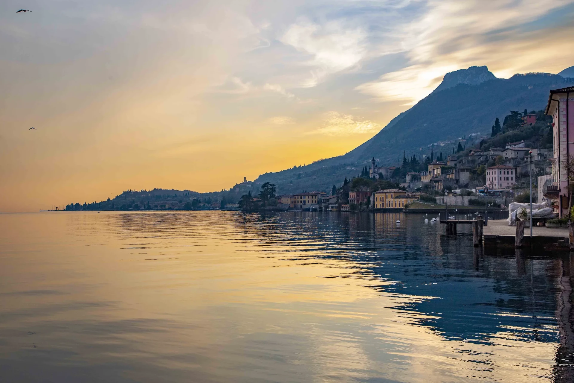 Gargnano's waterfront at sunset, with the village and mountains reflected in Lake Garda