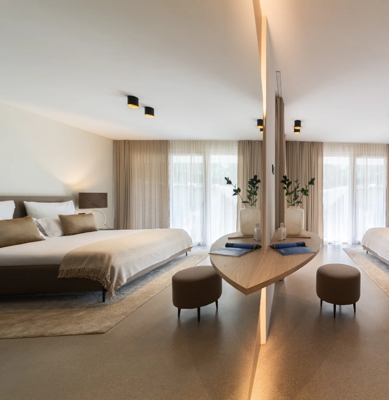 Double bedroom with king-size bed and sheer curtains, reflected in a tall backlit mirror beside a curved oak dressing table