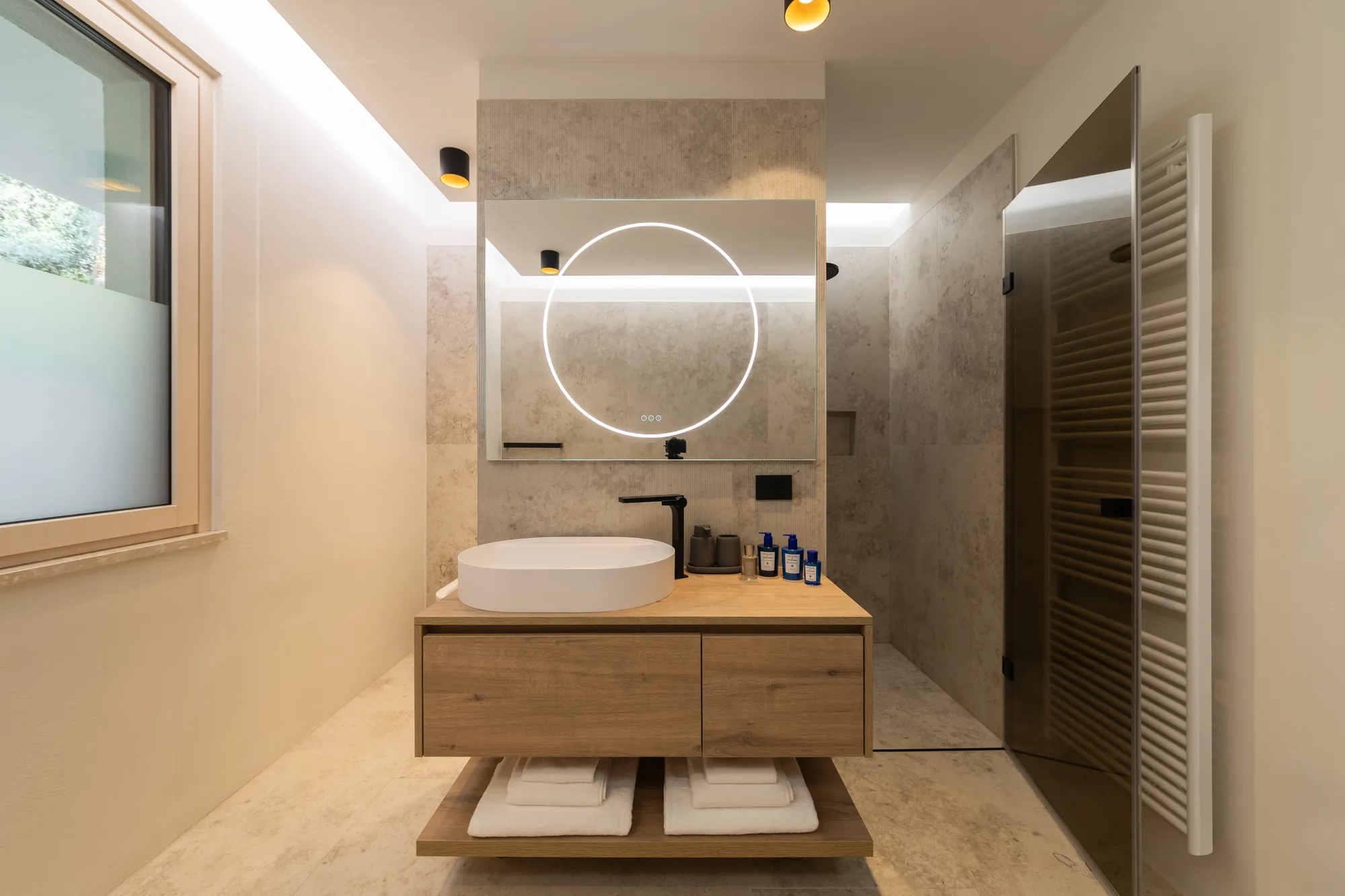 En-suite bathroom with illuminated round mirror and oak vanity