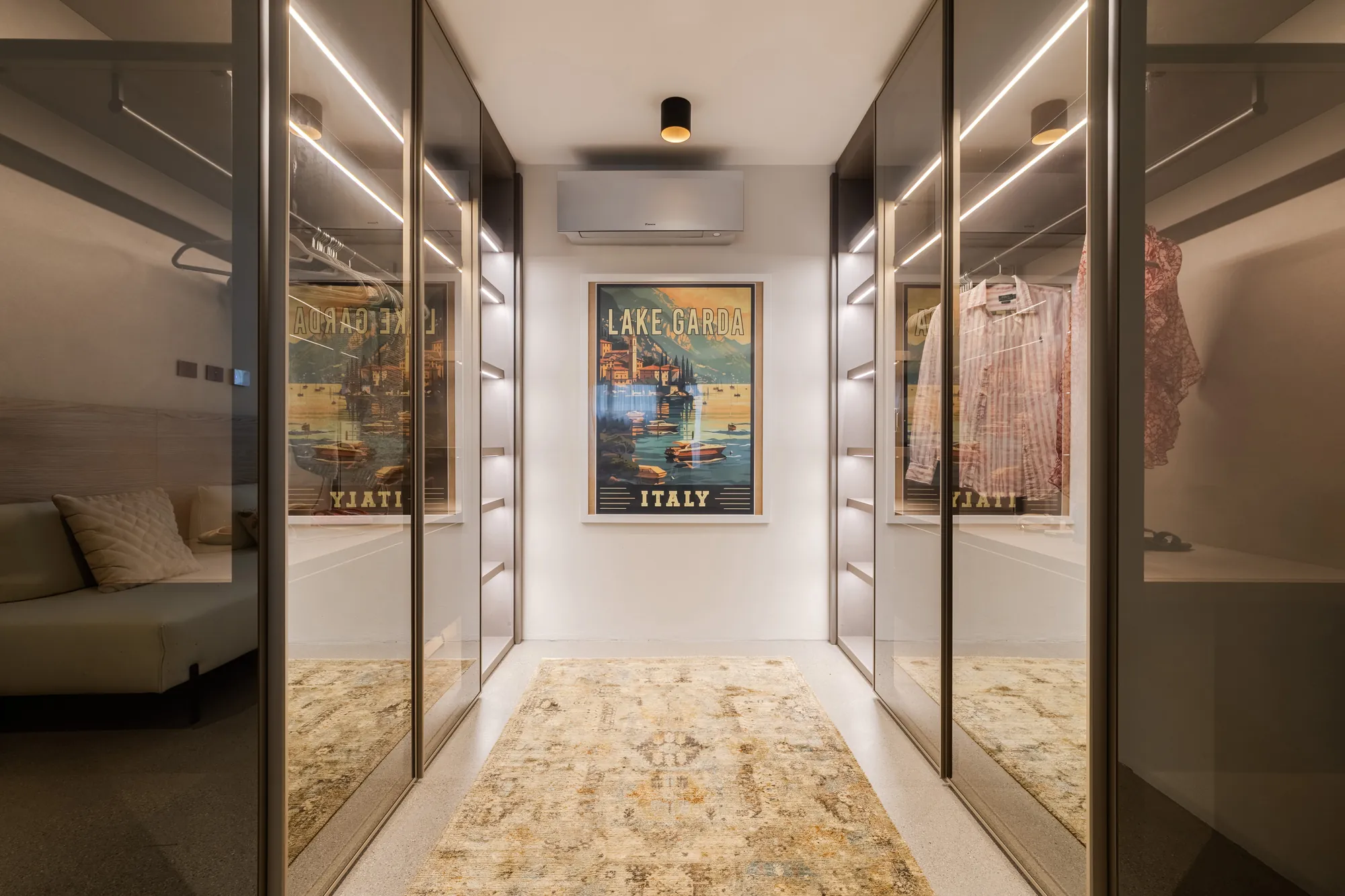 Walk-in closet with illuminated glass wardrobes and a Lake Garda poster