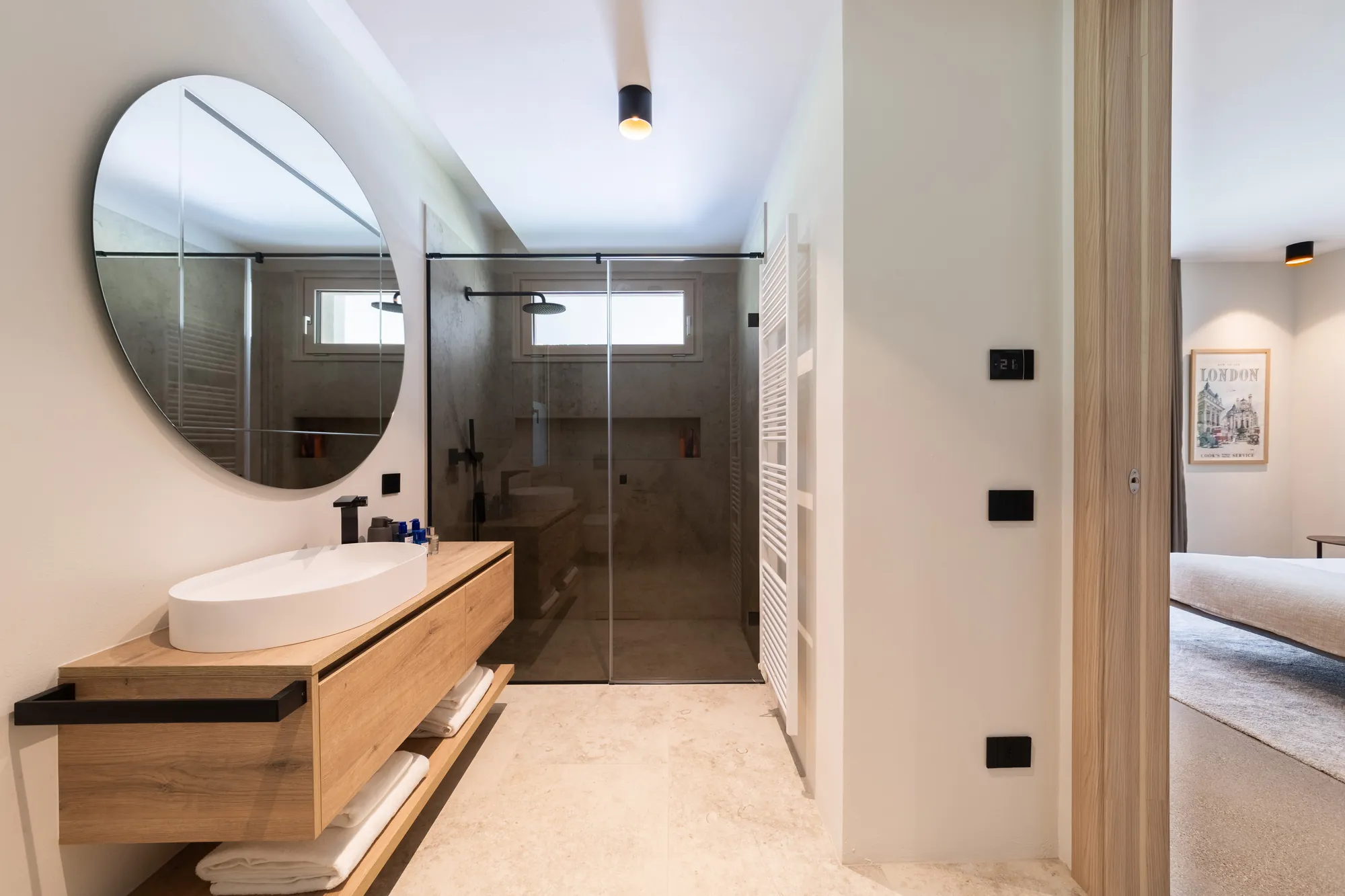 En-suite bathroom with oval basin, round mirror and glass walk-in shower